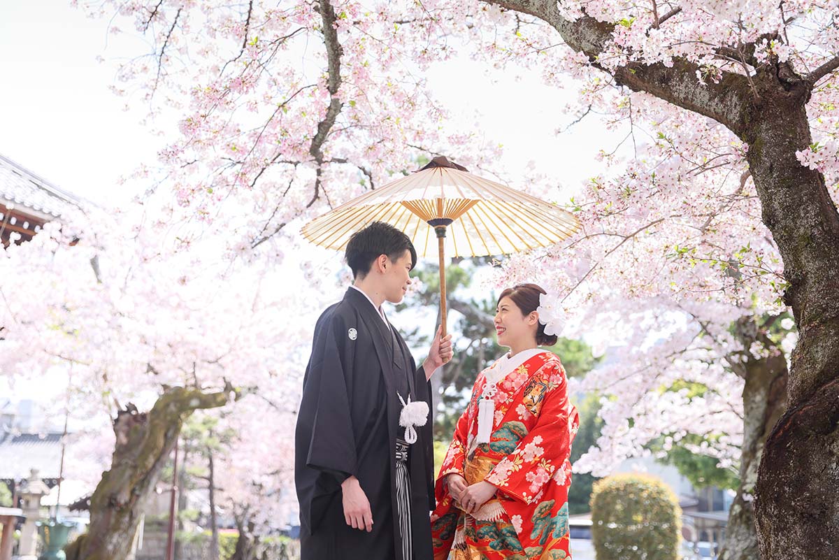 桜を背景に和傘の中で微笑み合う新郎新婦様
