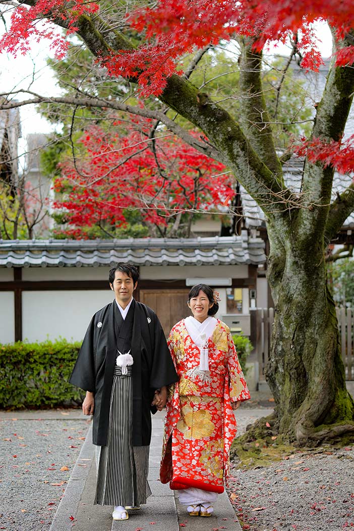 京都のお寺の境内で紅葉を背景に歩いている新郎新婦様