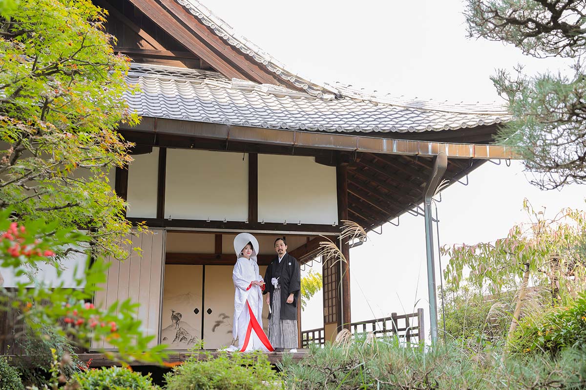 歴史的建造物を背景に綿帽子の姿の花嫁様と新郎様