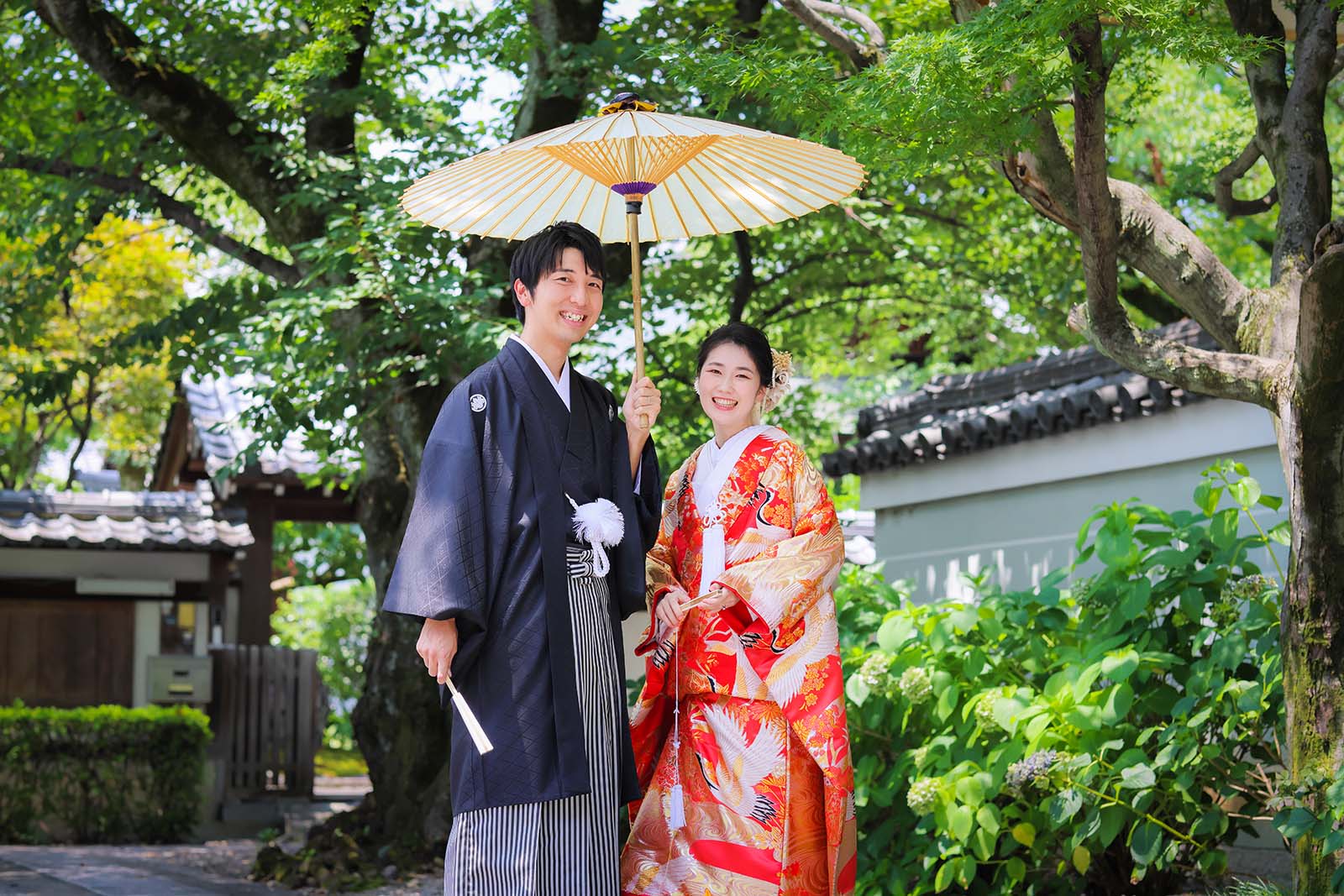 境内で緑を背景に番傘を使って鮮やかな結婚写真