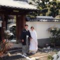塔頭寺院前の雪と腕を組んで笑顔の新郎新婦様。