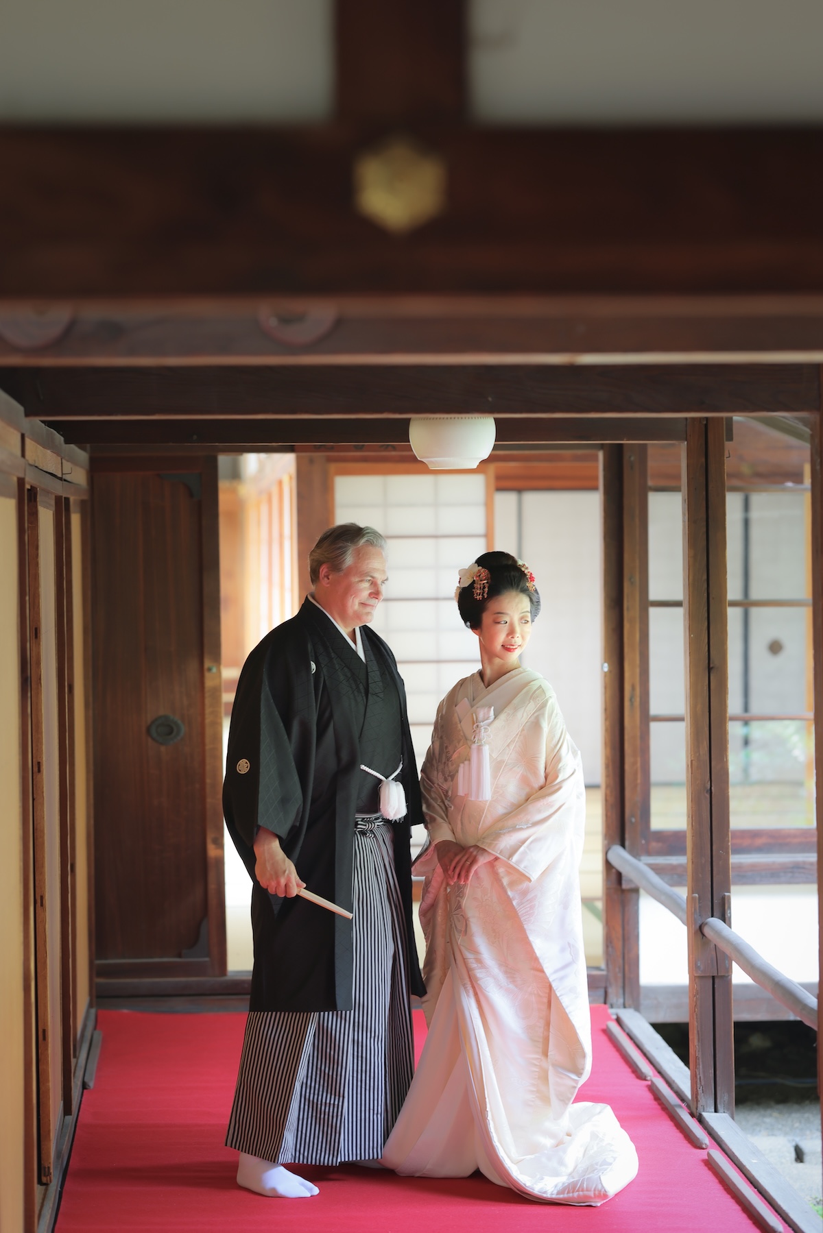 赤い毛氈の上で立ち姿の国際結婚の和装姿の新郎新婦様