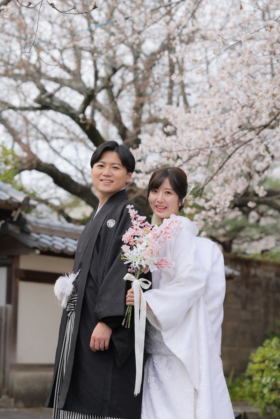 桜を背景に新郎様の背中に寄り添う花嫁様