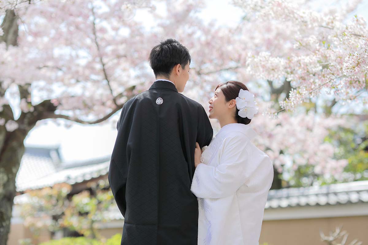 桜を背景に寄り添いあう新郎新婦様の後ろ姿