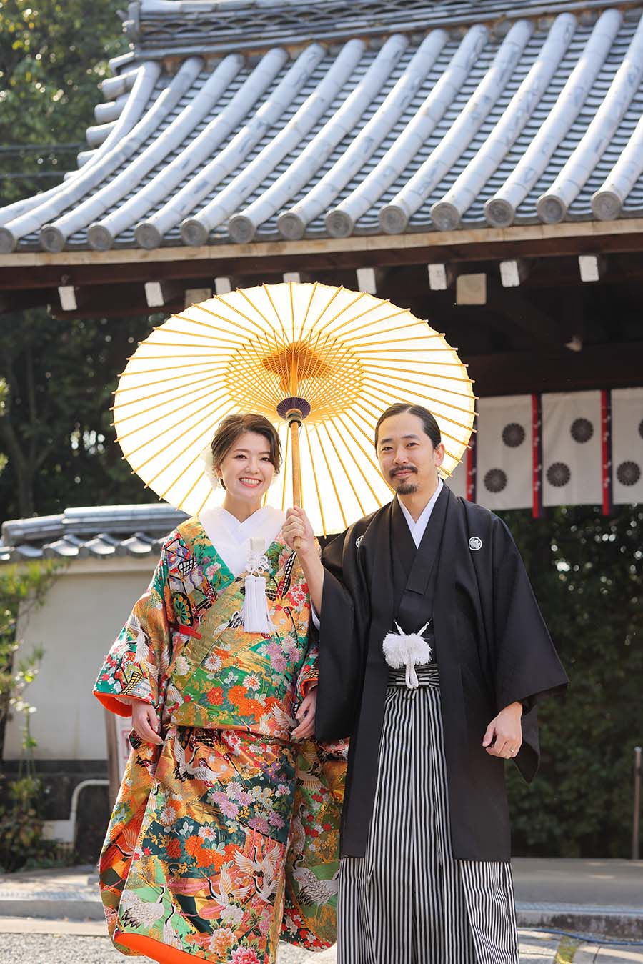 京都のお寺の山門を背景に和傘を持ってある区新郎新婦様