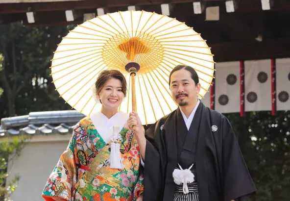 京都のお寺の山門を背景に和傘を持ってある区新郎新婦様
